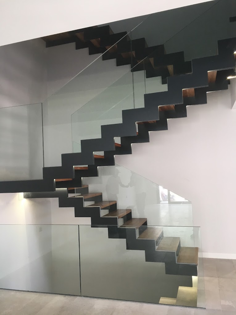 Escalera metálica suspendida con peldaños de madera y barandilla de vidrio
